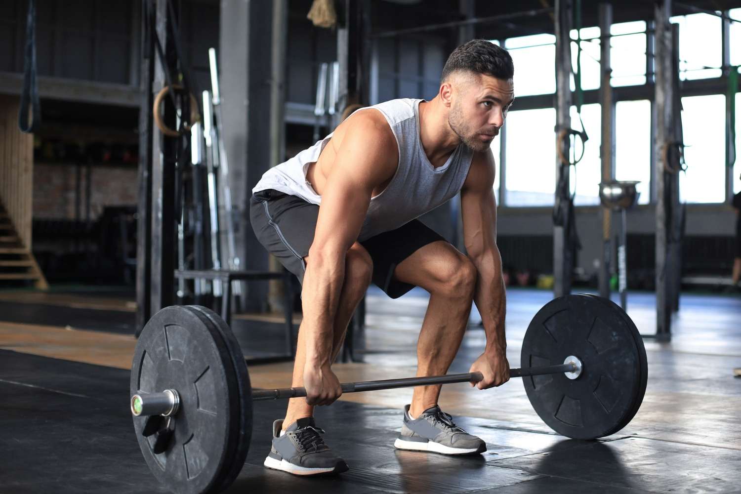 Muscular man in a gym crouched at a loaded barbell preparing for a deadlift